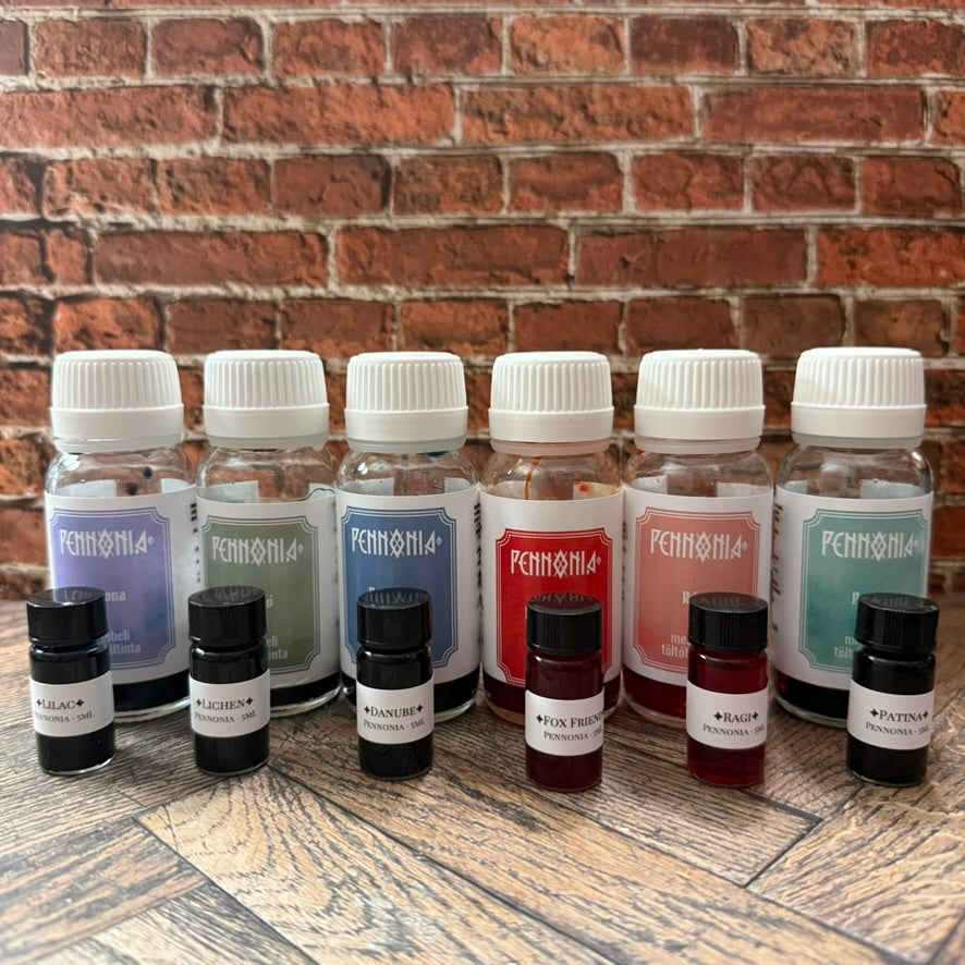 Six 5 mL Pennonia sample vials in front of the full 60 mL Pennonia bottles they were decanted from (bottles not included)