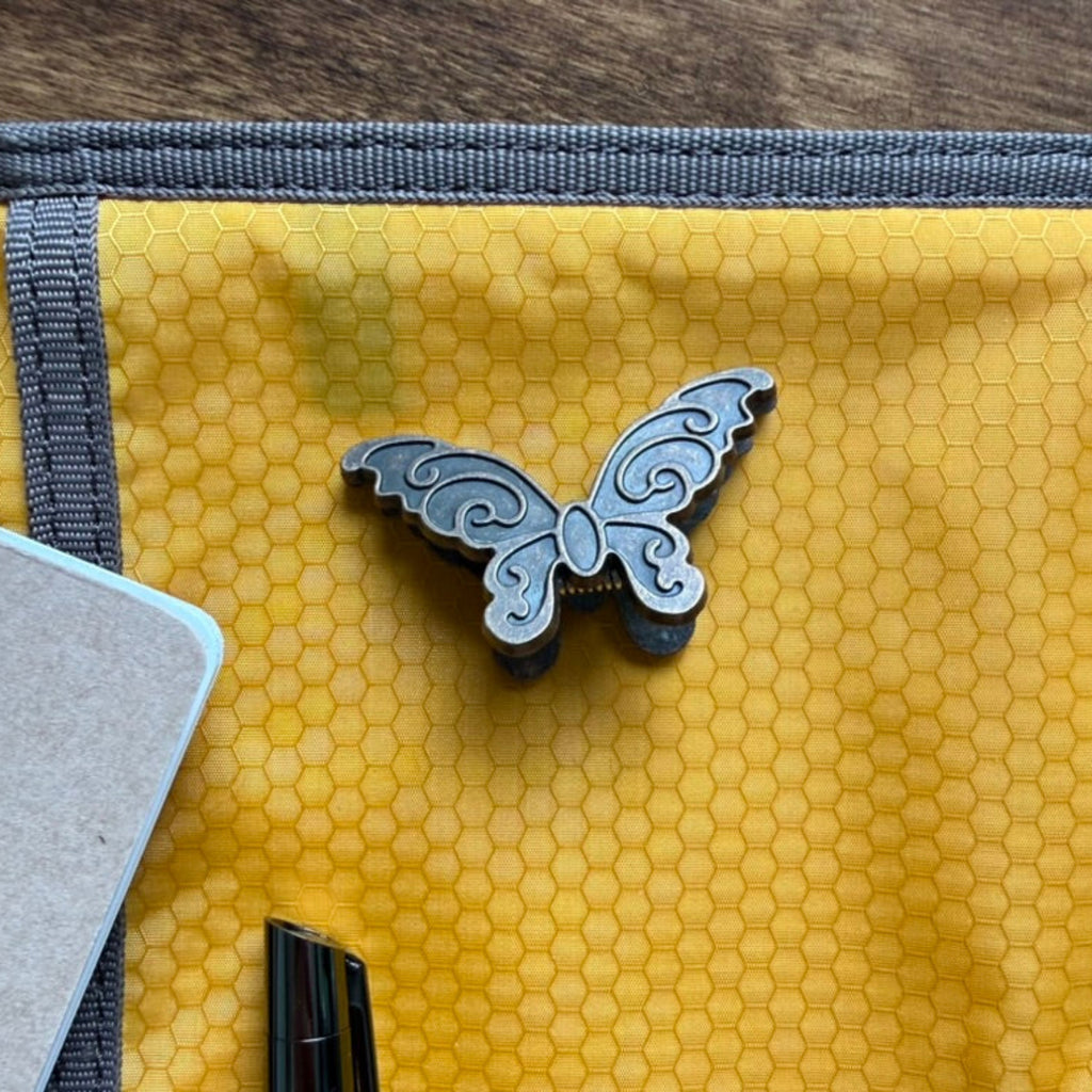 Antique brass butterfly journal clip resting on a yellow notebook case