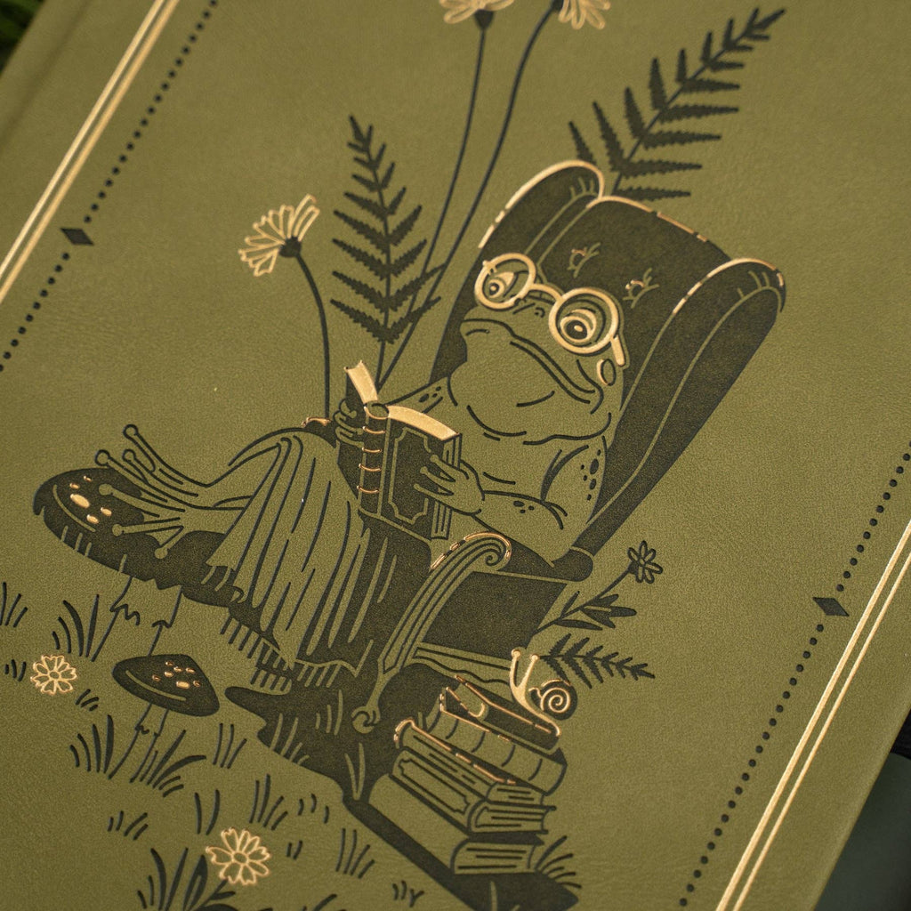 Archer & Olive Literary Frog B5 notebook: Close-up of the reading frog, armchair, and gold botanical details.