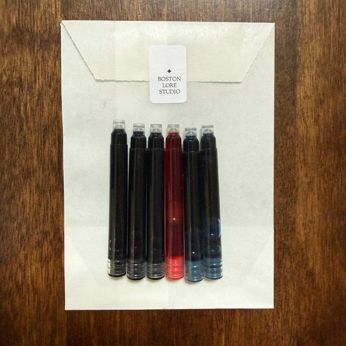 Assorted black blue and red short international fountain pen ink cartridges with Boston Lore Studio glassine envelope