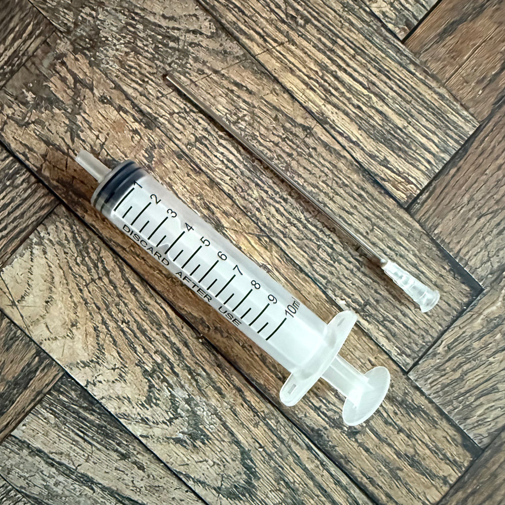 10 mL ink syringe with extra-long blunt metal needle resting on a wood surface