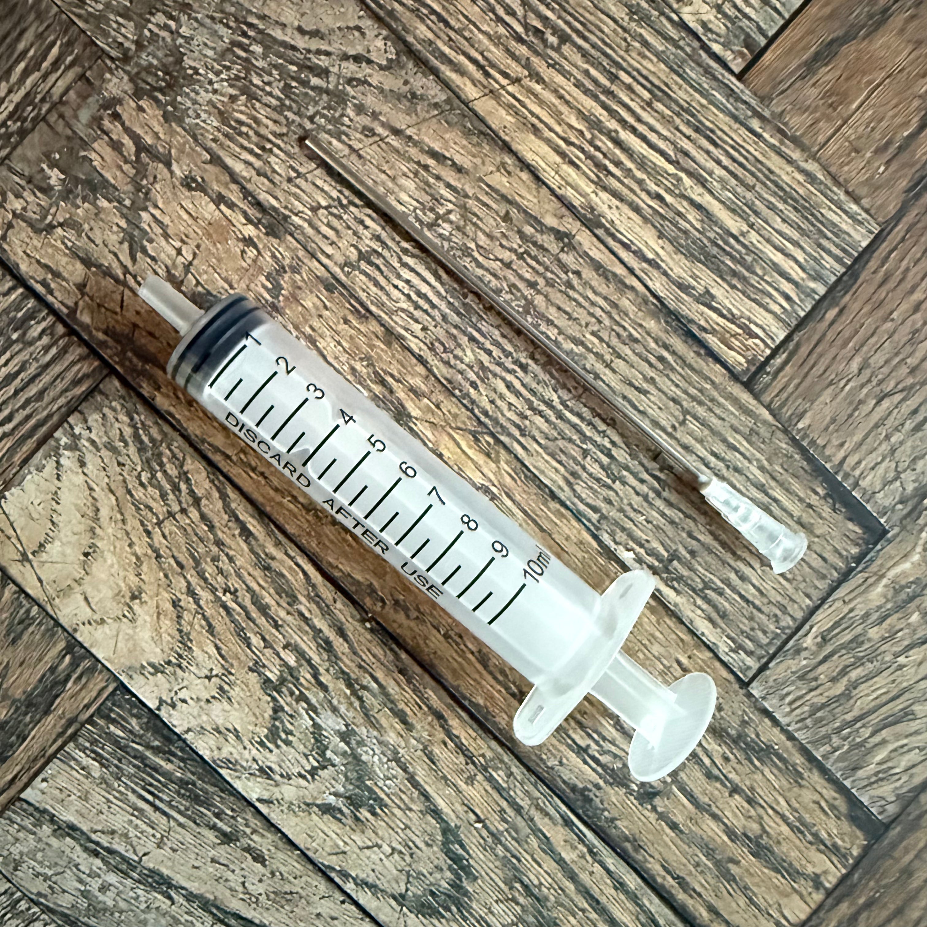 10 mL ink syringe with extra-long blunt metal needle resting on a wood surface