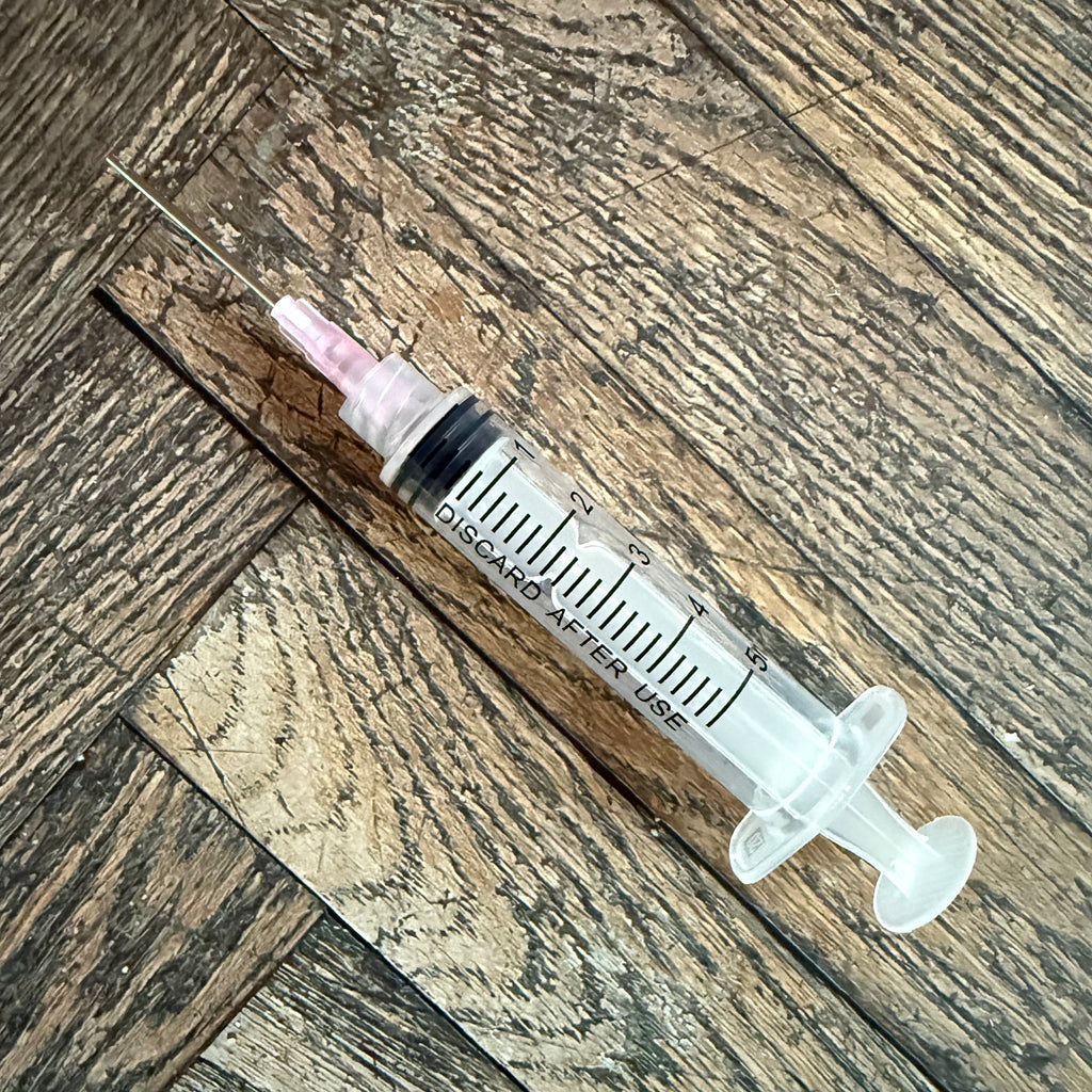 5 mL ink syringe with attached blunt-tip needle resting on a wood surface