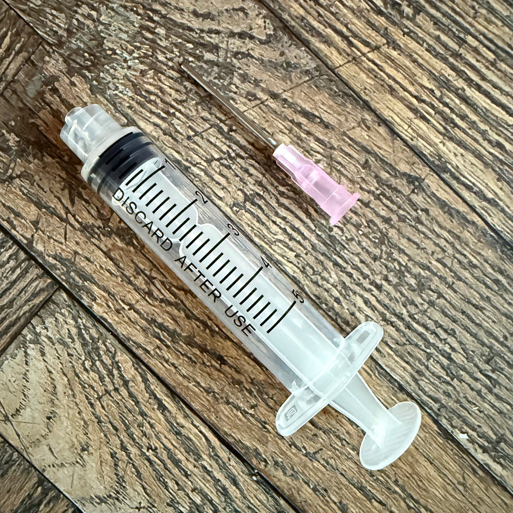 5 mL ink syringe beside its detached pink-hub blunt-tip needle on a wood surface