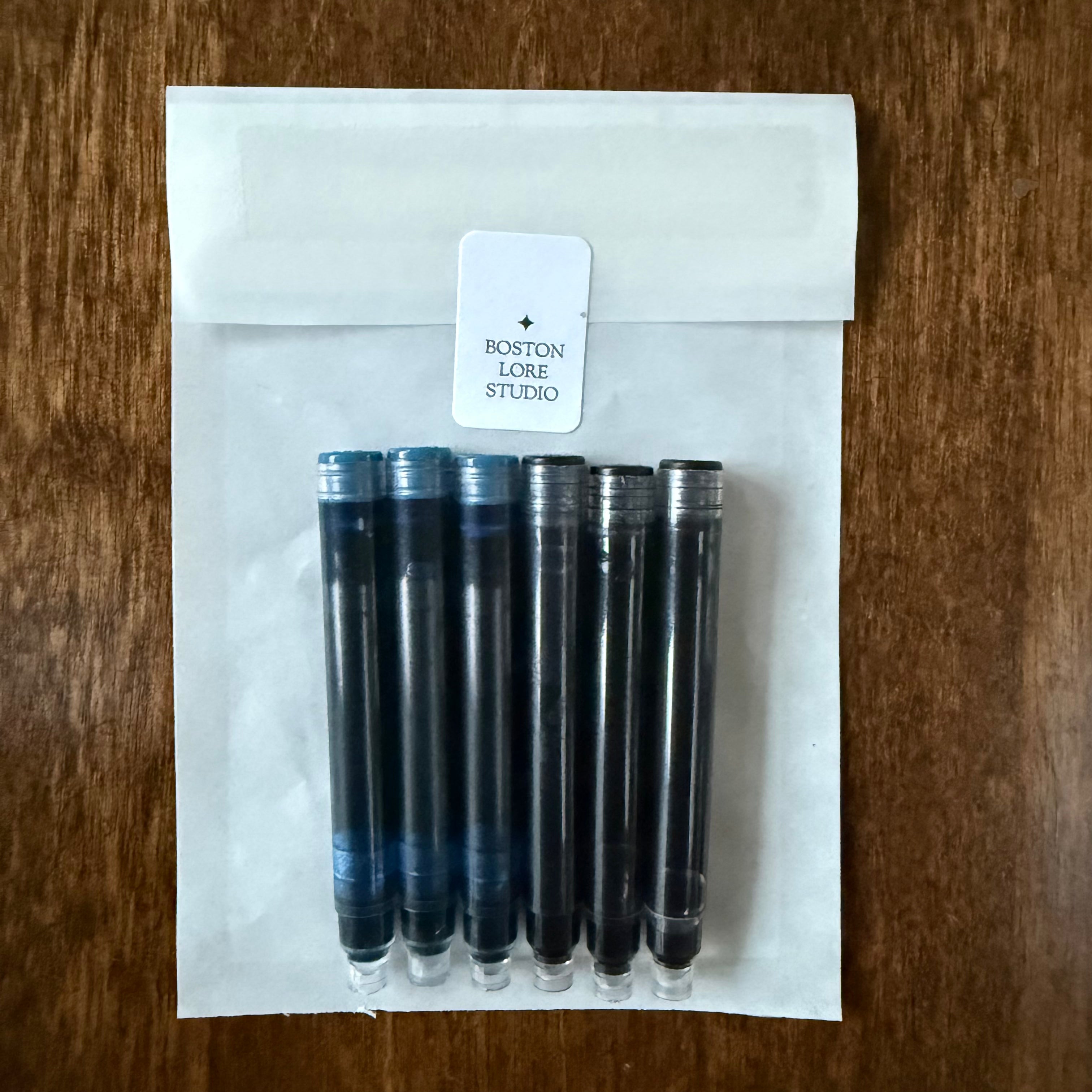 Three blue-black and three black international fountain pen ink cartridges in a Boston Lore Studio glassine envelope