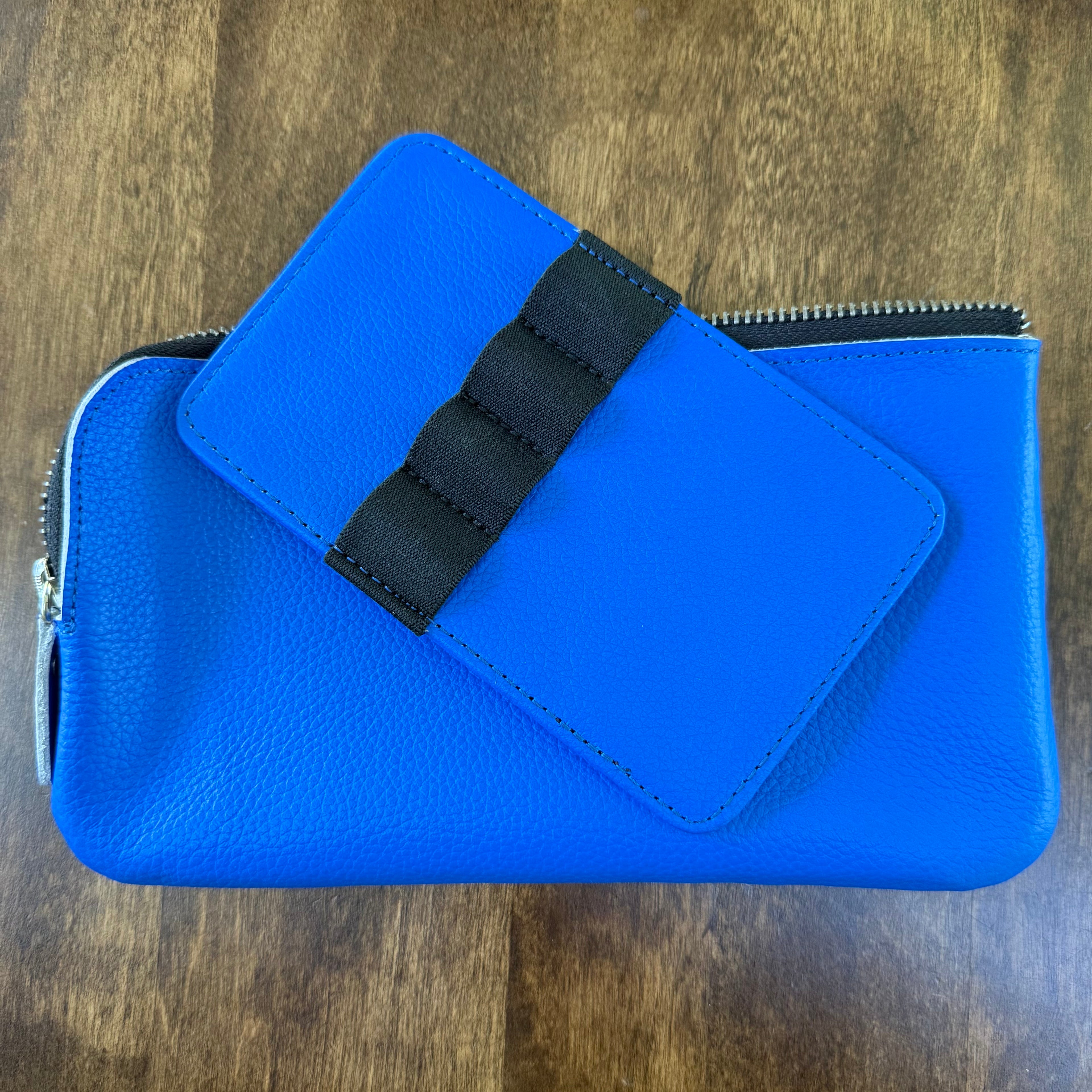 Empty removable blue leather pen insert with four black elastic loops resting on the matching zippered pouch.