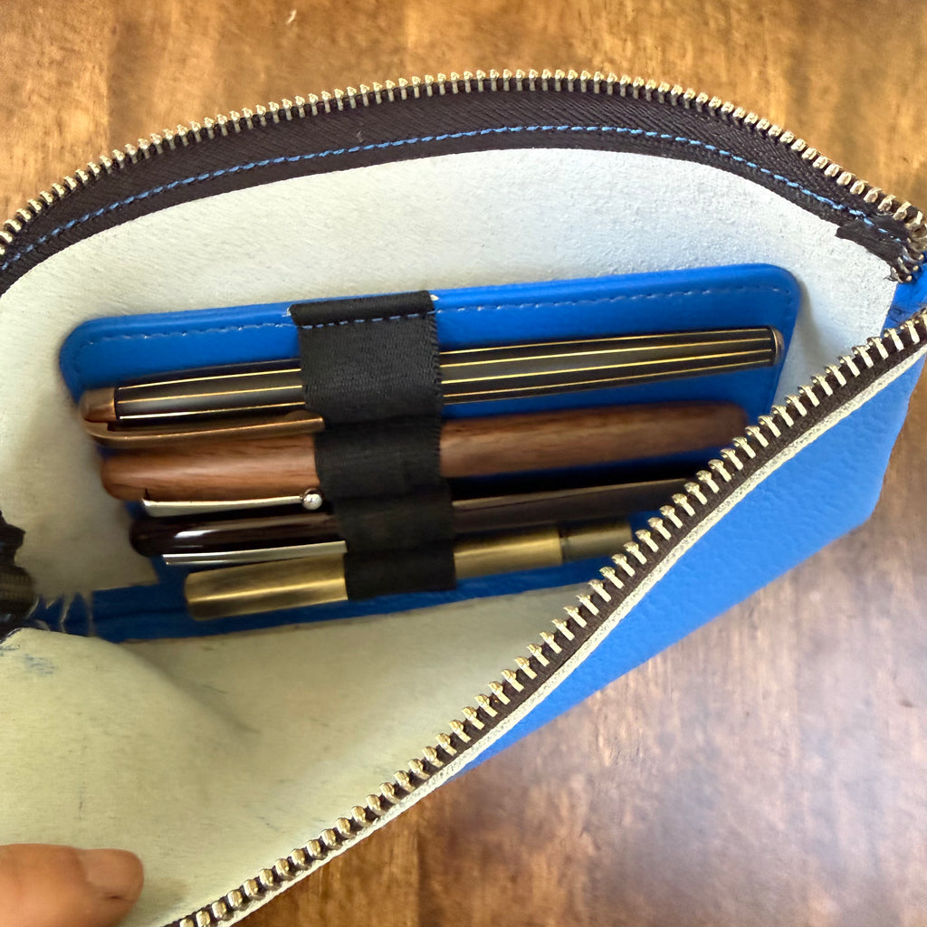 Open blue leather pen case showing its light-colored interior and removable insert holding four pens.