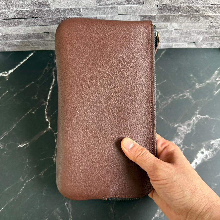 Closed espresso brown cowhide leather pen case held upright in one hand, showing its size and pebbled leather grain
