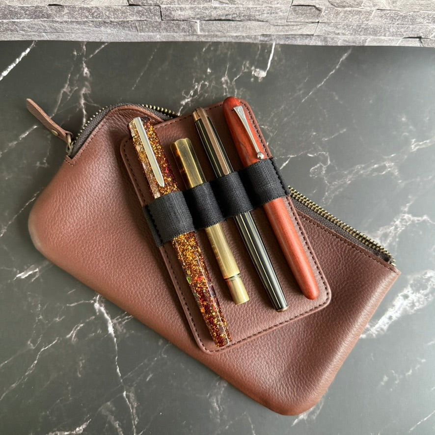 Leather pen insert holding four fountain pens in black elastic loops, resting on the espresso brown zipper case