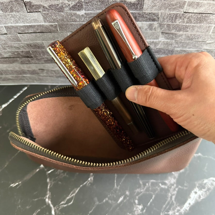 Hand lifting the removable four-pen leather insert out of the open espresso brown zipper case