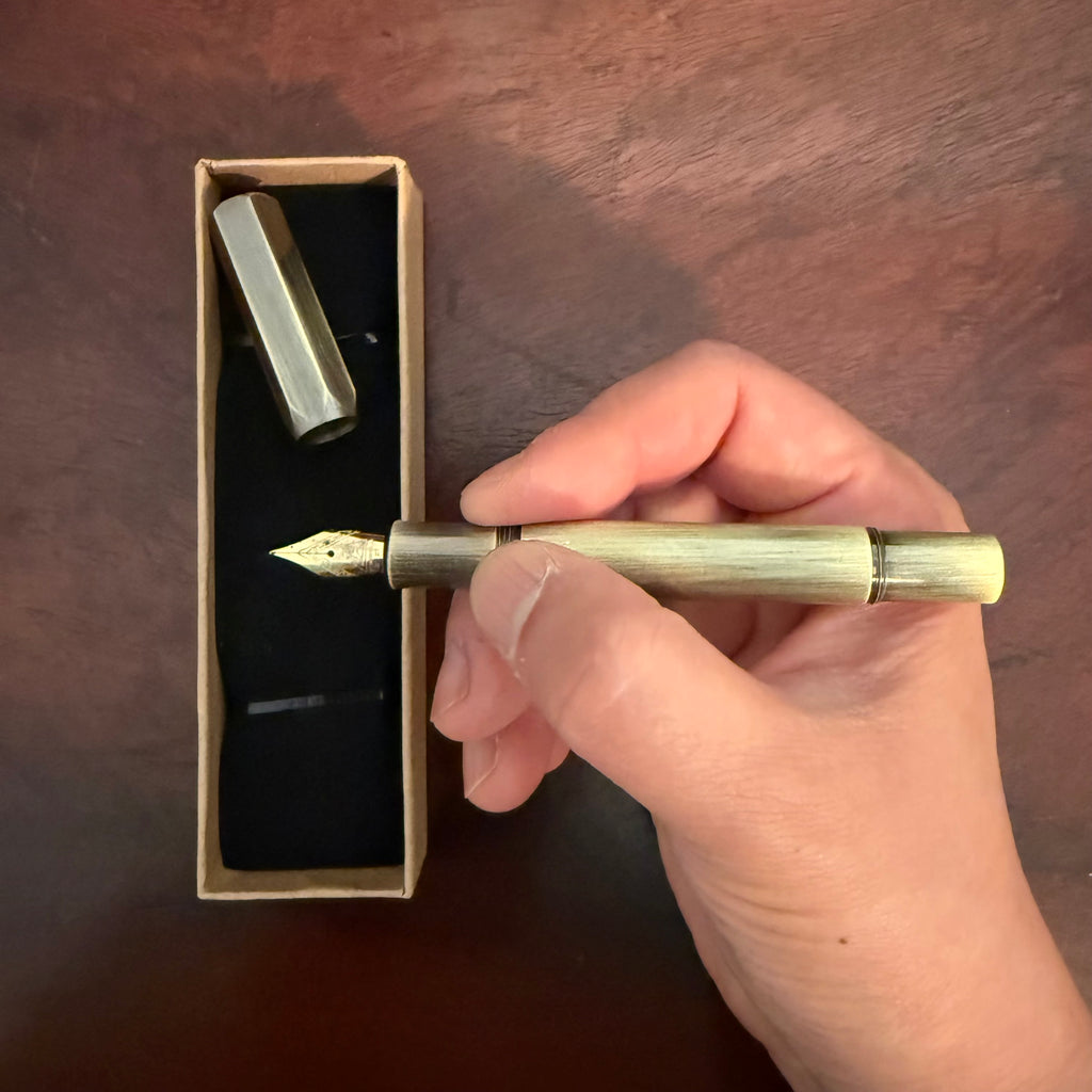Compact brushed brass pocket fountain pen presented in a kraft paper box with black insert.