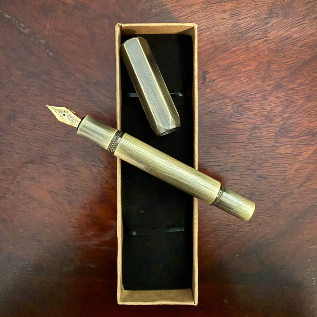 Compact brushed brass pocket fountain pen presented in a kraft paper box with black insert
