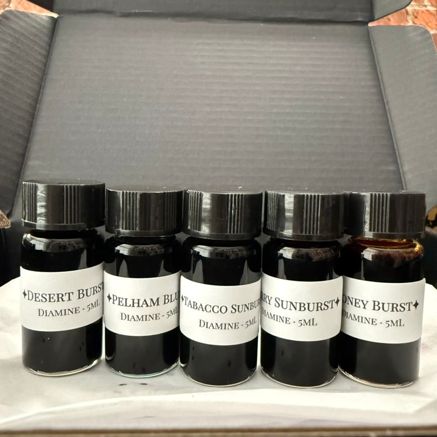 Close-up of five labeled Diamine Guitar series ink vials standing in a gift box: Desert Burst, Pelham Blue, Tobacco Sunburst, Cherry Sunburst and Honey Burst