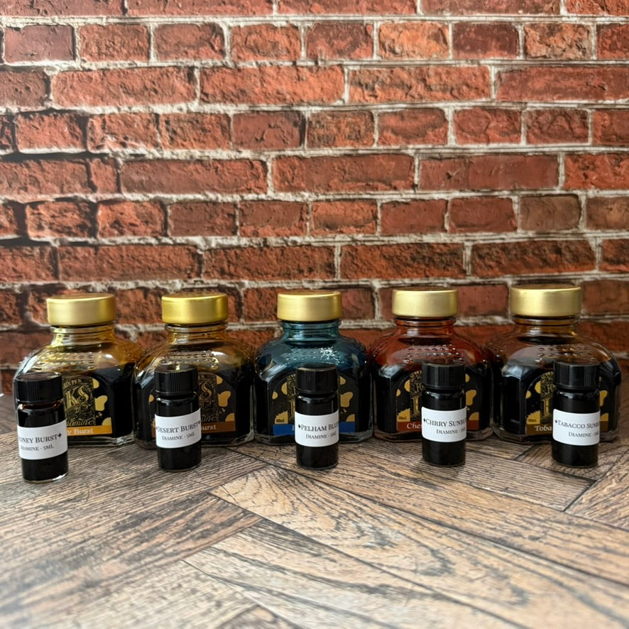 Five Diamine Guitar series 5 mL sample vials lined up in front of their full 80 mL source bottles