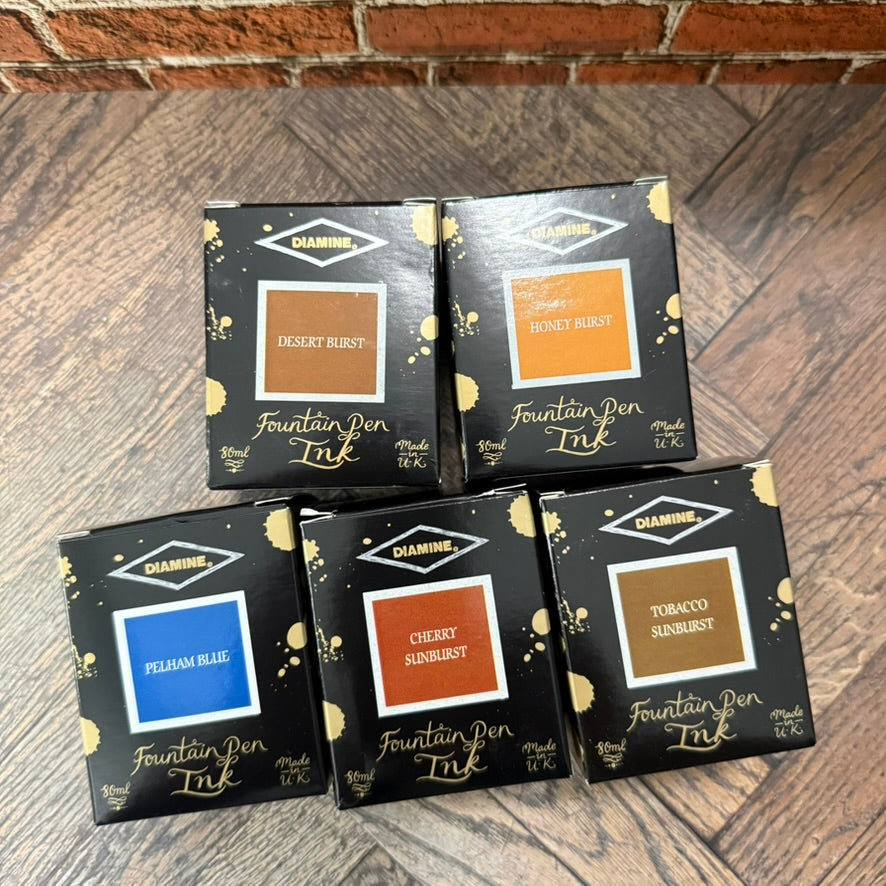 Boxes of the five Diamine Guitar series 80 mL inks used for the sampler: Desert Burst, Honey Burst, Pelham Blue, Cherry Sunburst and Tobacco Sunburst