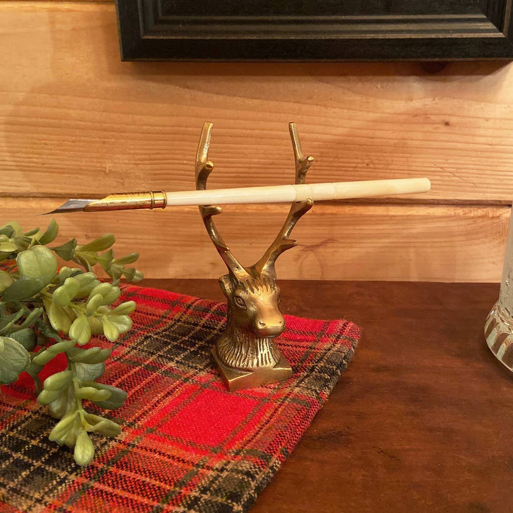 Antiqued brass stag pen holder supporting a dip pen on a wooden desk; pen not included
