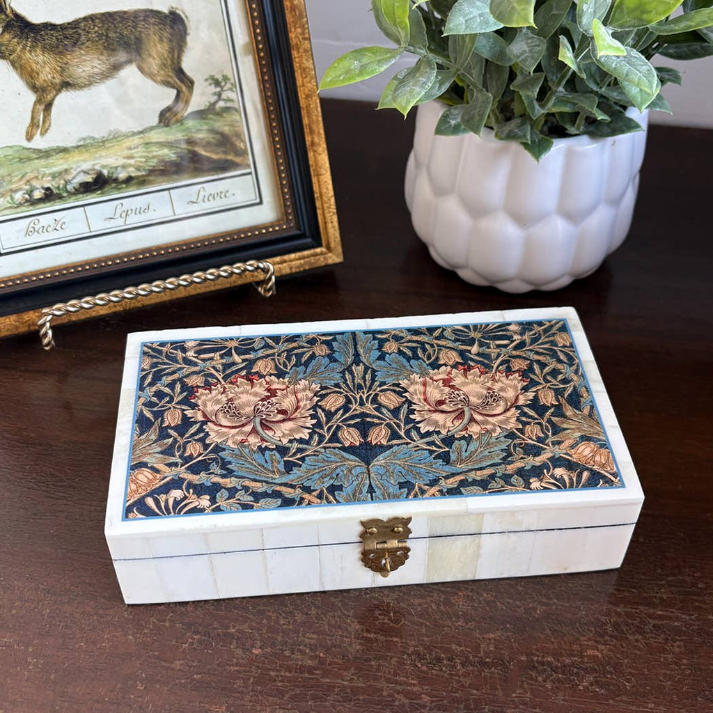 William Morris floral keepsake box on a wooden desk beside a plant and framed picture