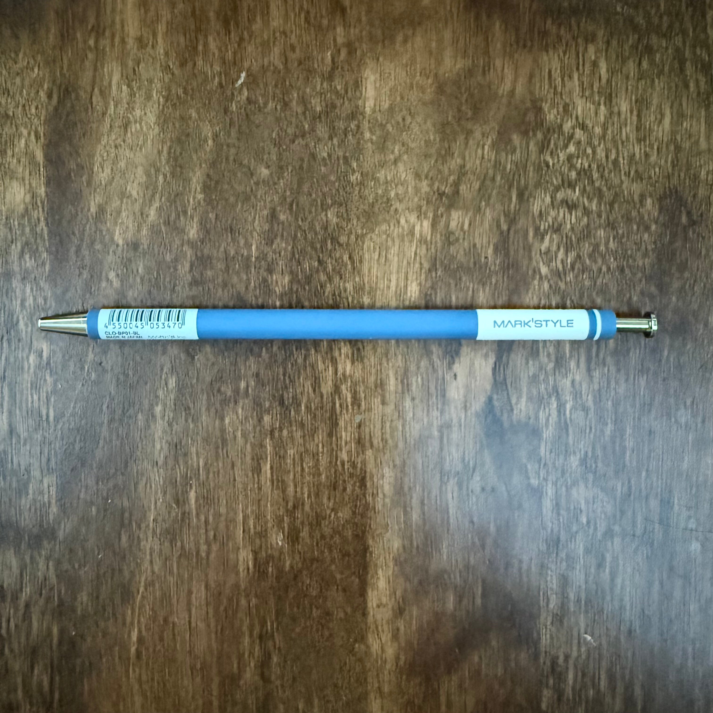 MARK’S COLORS blue gel pen lying horizontally on a wooden surface, with the white MARK’STYLE panel facing upward.