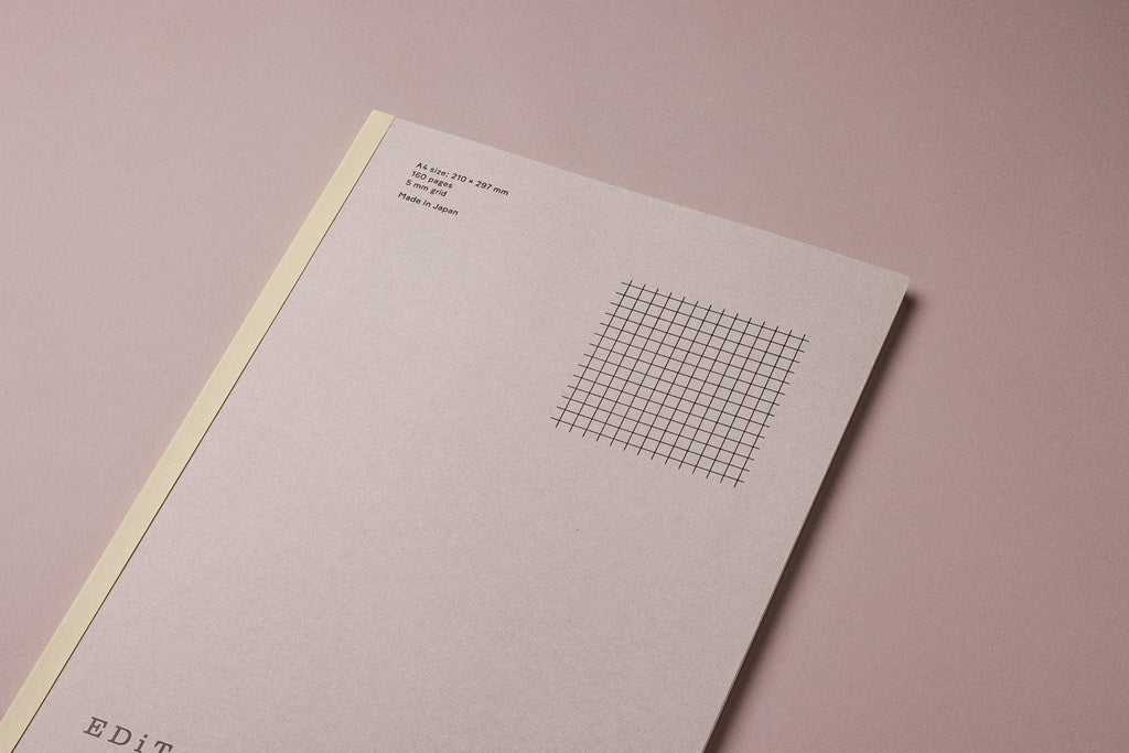 Angled view of the MARK’S EDiT A4 pale gray notebook cover, showing the yellow spine and printed grid illustration.