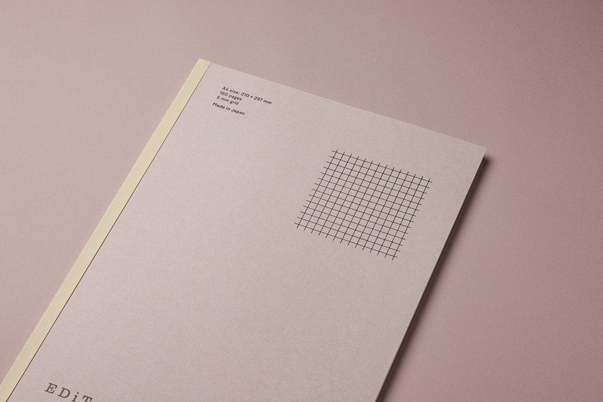 Angled view of the MARK’S EDiT A4 pale gray notebook cover, showing the yellow spine and printed grid illustration.