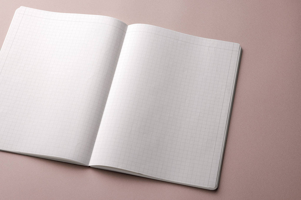 Open MARK’S EDiT A4 notebook showing fine gray grid ruling and rounded page corners on a muted pink background.