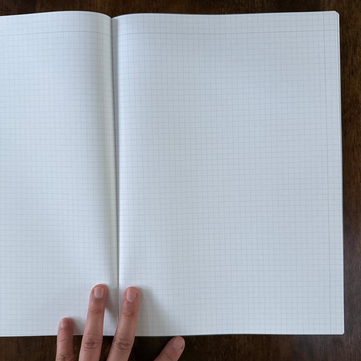 MARK’S EDiT A4 notebook held open on a wooden desk, showing a spacious two-page spread of light gray 5 mm grid ruling.