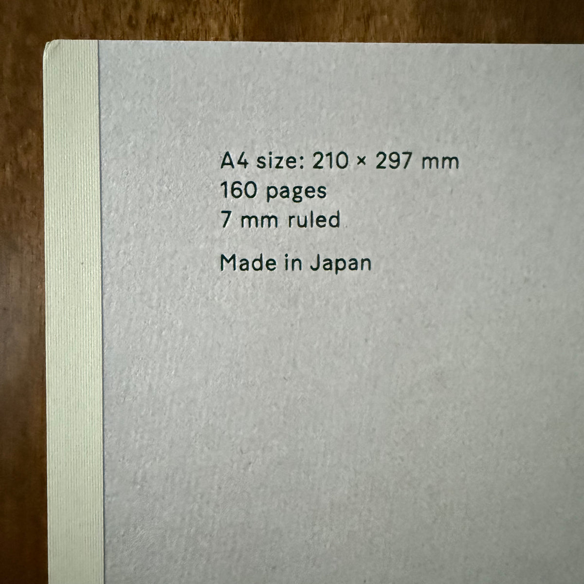 Close-up of the textured gray cover and pale spine, showing A4 dimensions, 160 pages, 7 mm ruling, and Made in Japan.