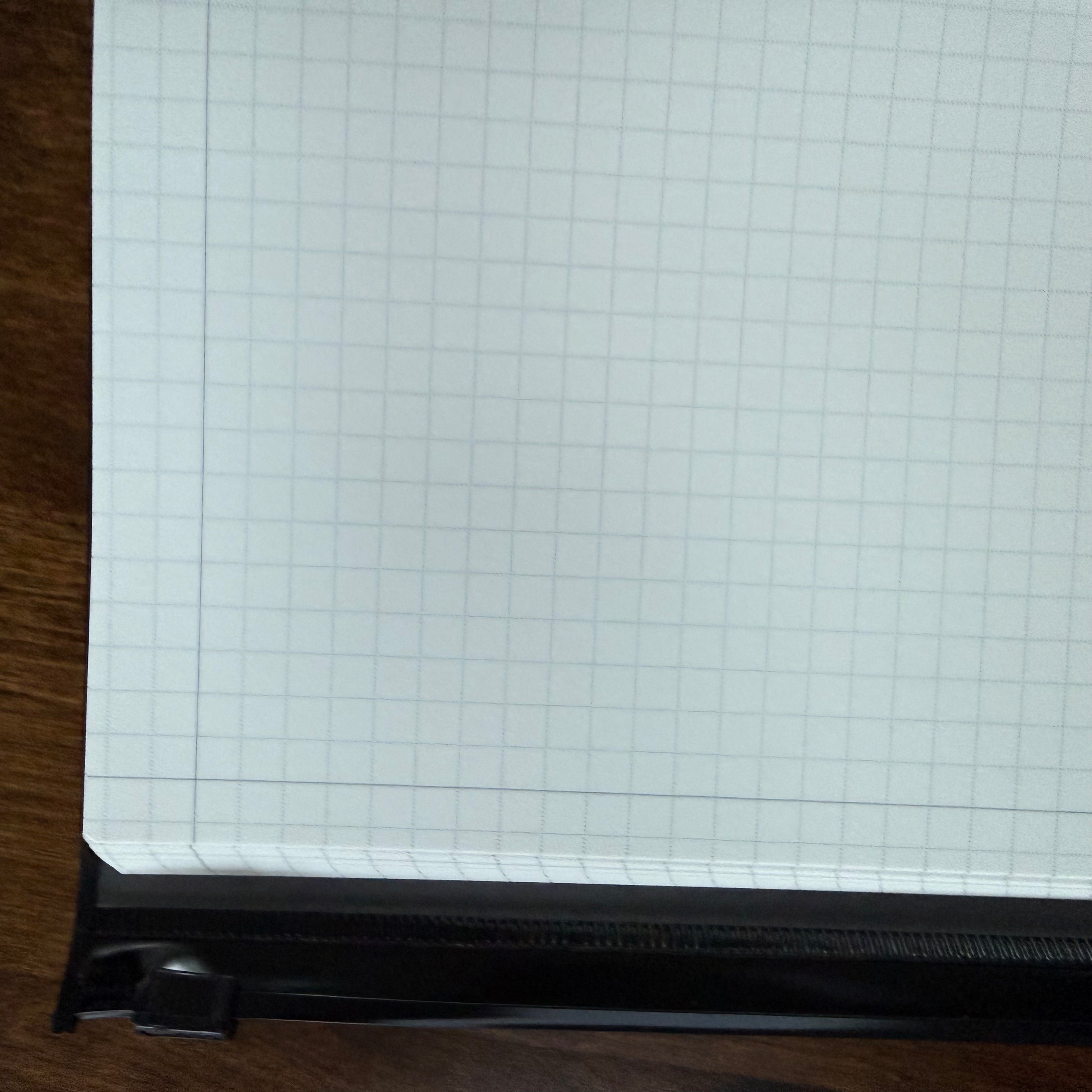 Close-up of the MARK’S EDiT B6 notebook’s light gray grid paper, page edges, and black zipper cover.
