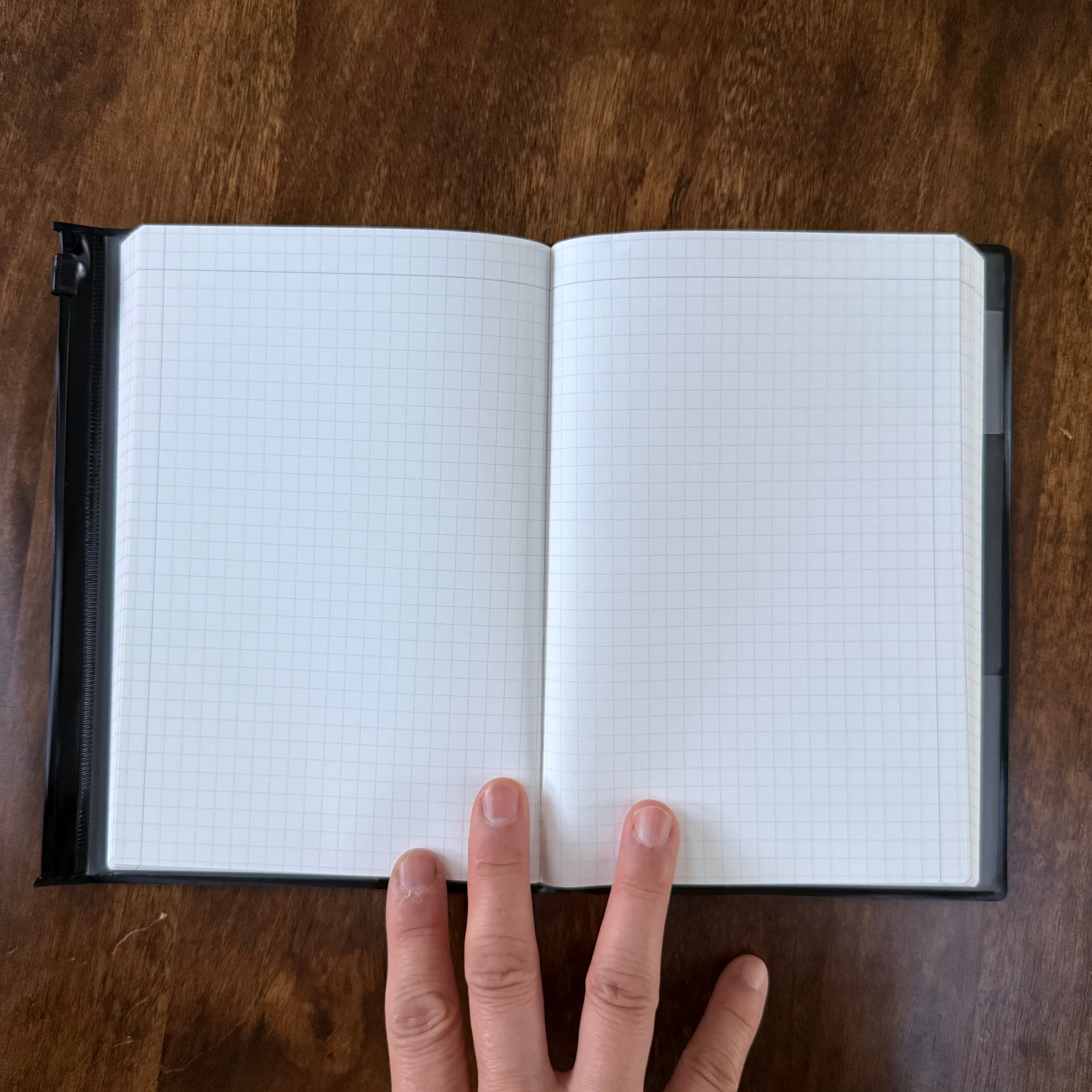 MARK’S EDiT B6 Midnight Black notebook held open on a wooden surface, showing a two-page spread of light gray grid ruling.
