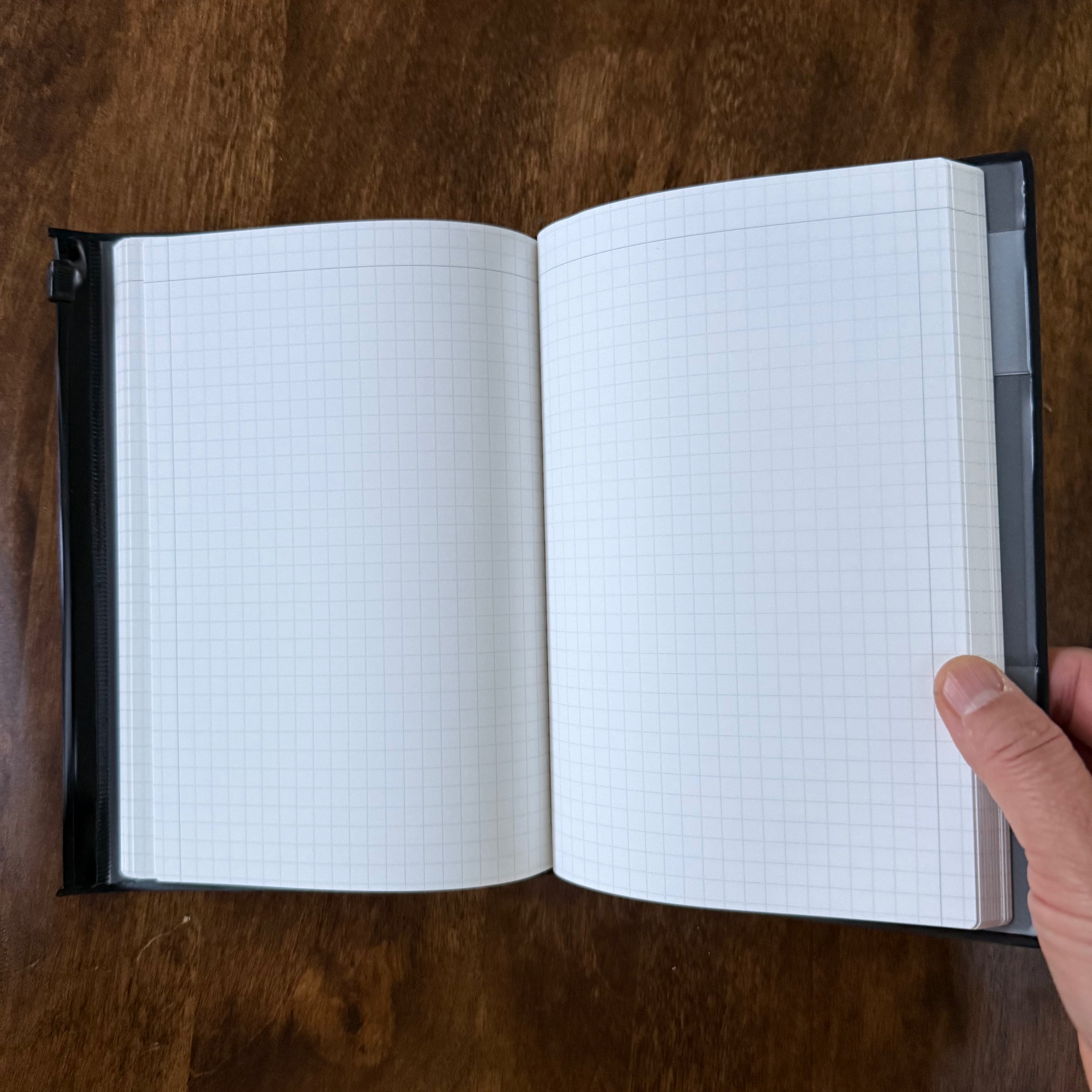 MARK’S EDiT B6 Midnight Black notebook held open at the outer edge, showing its grid pages and center binding.