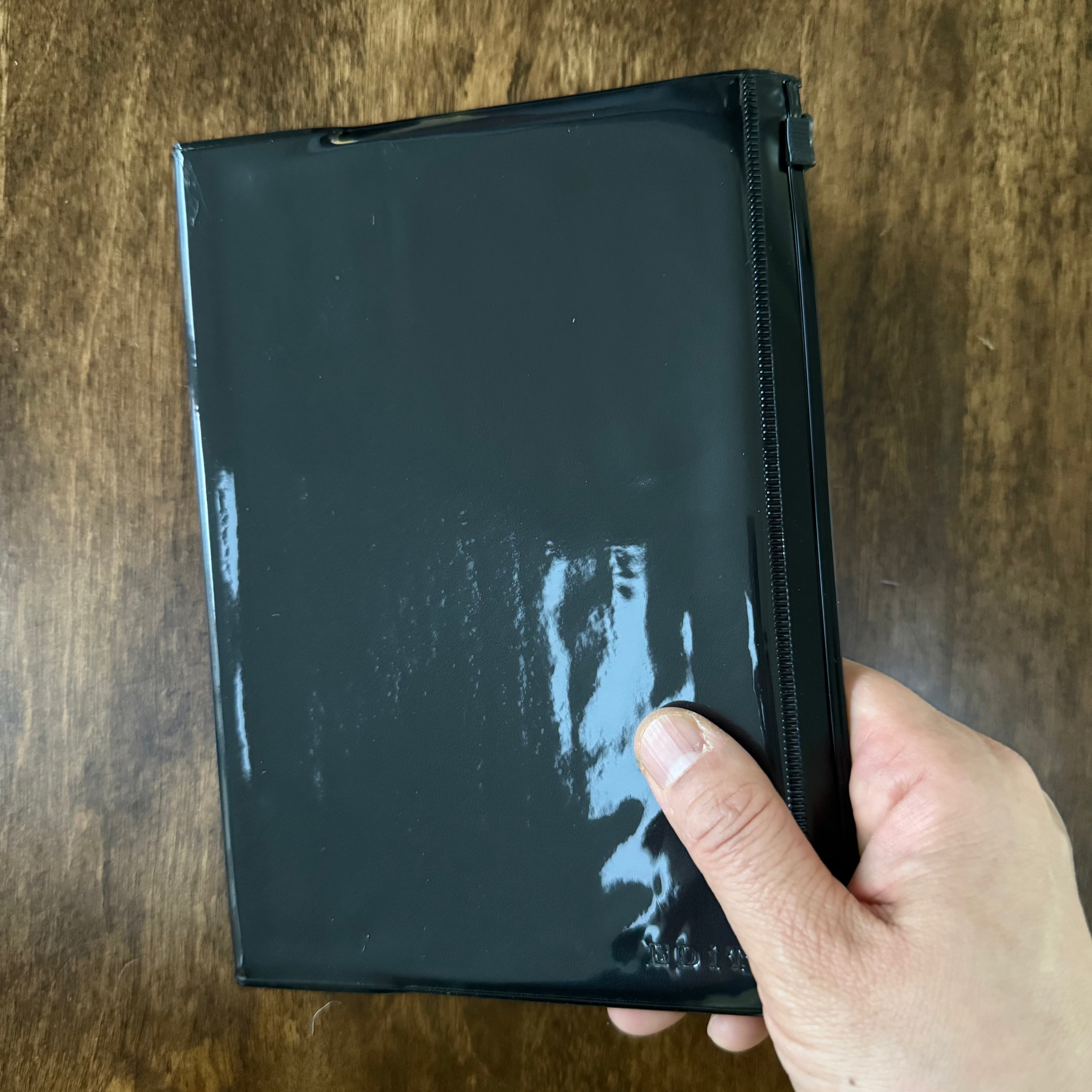 MARK’S EDiT B6 Midnight Black notebook held in one hand, showing its glossy cover and slide-zip front pocket.
