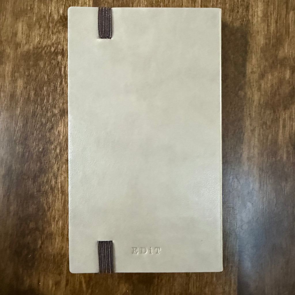 Back of the MARK’S EDiT B7 Light Latte notebook showing the embossed EDiT logo and elastic band attachment points.
