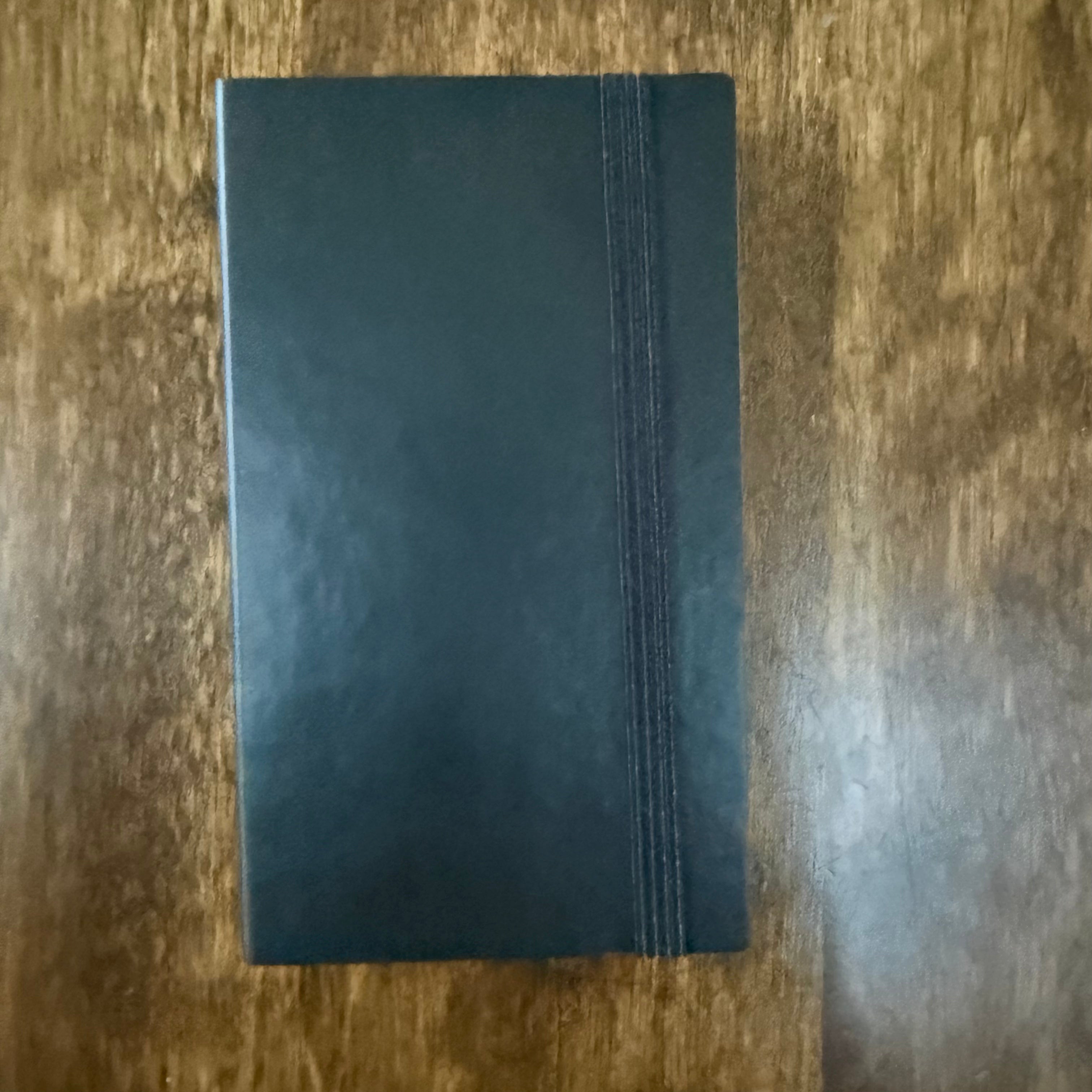 MARK’S EDiT B7 Midnight Black notebook on a wooden surface, showing the closed cover and black elastic band.