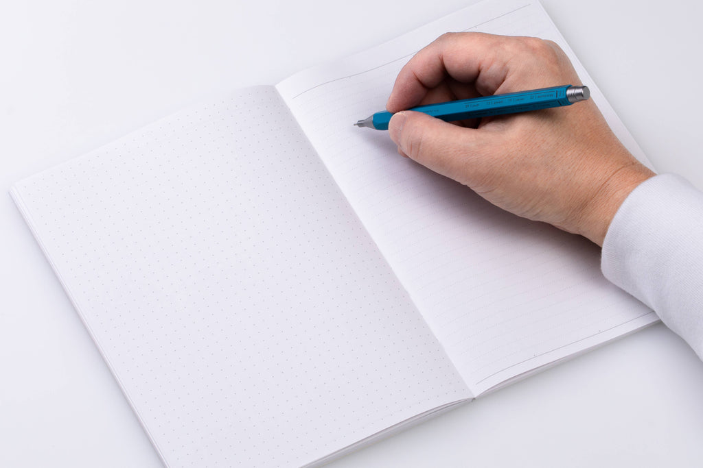 Open MARK'S Storage.it A5 notebook with dot-grid paper on the left and ruled paper on the right, shown with a person writing