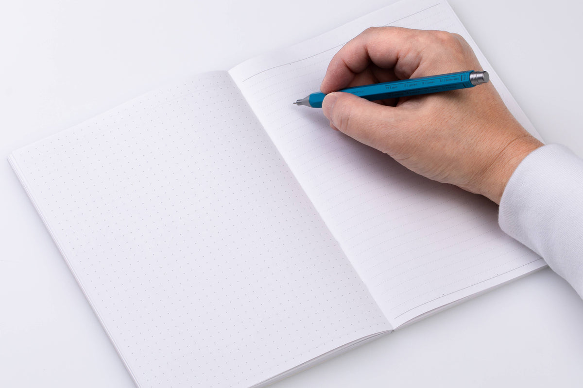 Open MARK'S Storage.it A5 notebook with dot-grid paper on the left and ruled paper on the right, shown with a person writing