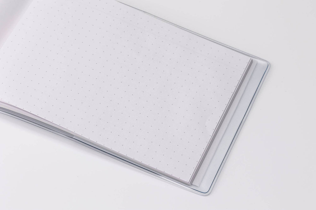 Close-up of the white dot-grid pages in a MARK'S Storage.it Desk notebook, shown inside a clear cover