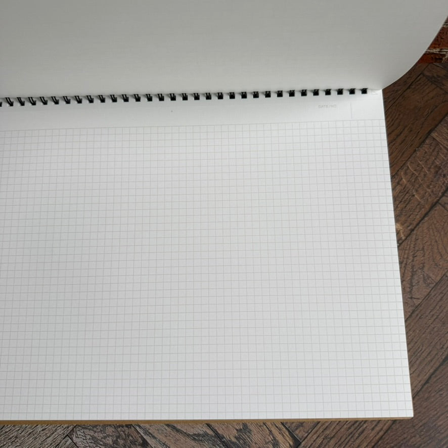 Open Maruman Mnemosyne A4 notebook showing a white page with a pale 5 mm grid below the twin-wire binding