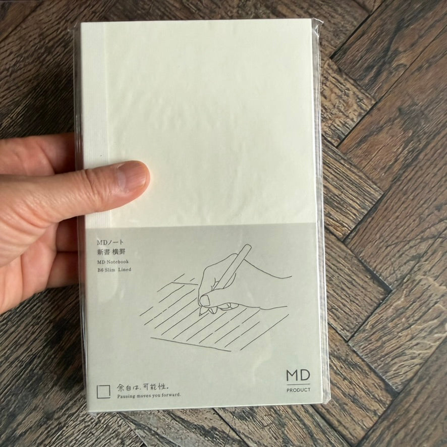Hand holding the Midori MD B6 Slim lined notebook to show its slim paperback size