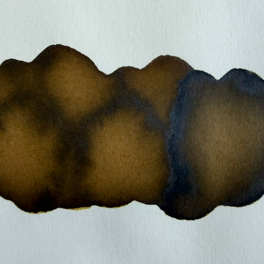 Close-up of a Nahvalur Saddle Amber ink swatch on Tomoe River 68 gsm paper showing golden amber-brown areas and darker pooling along the edges.