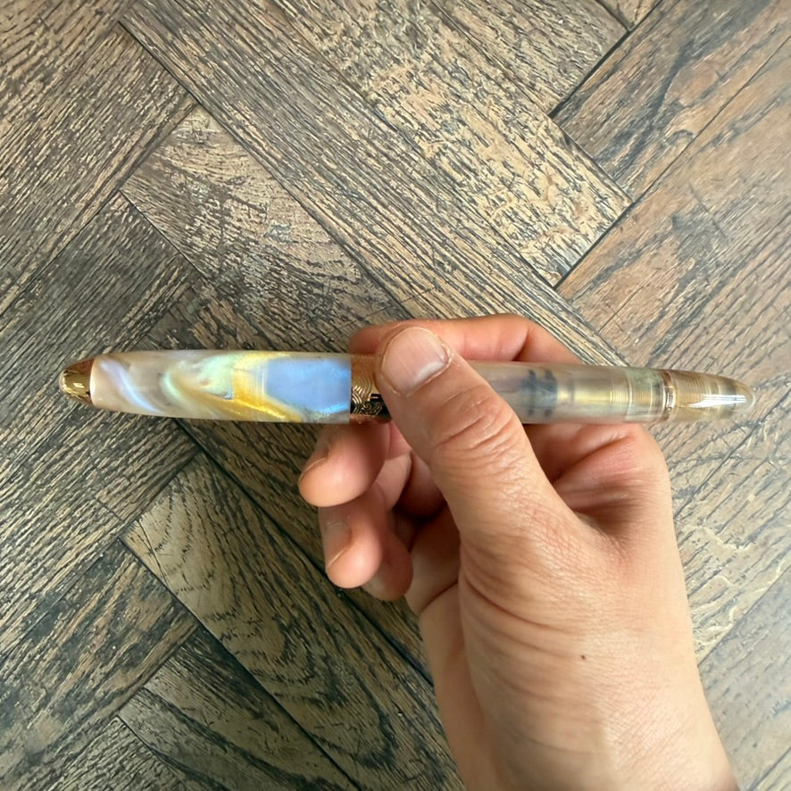 Hand holding the capped Nahvalur Horizon Pearl, showing the swirling pearl, gold and blue acrylic