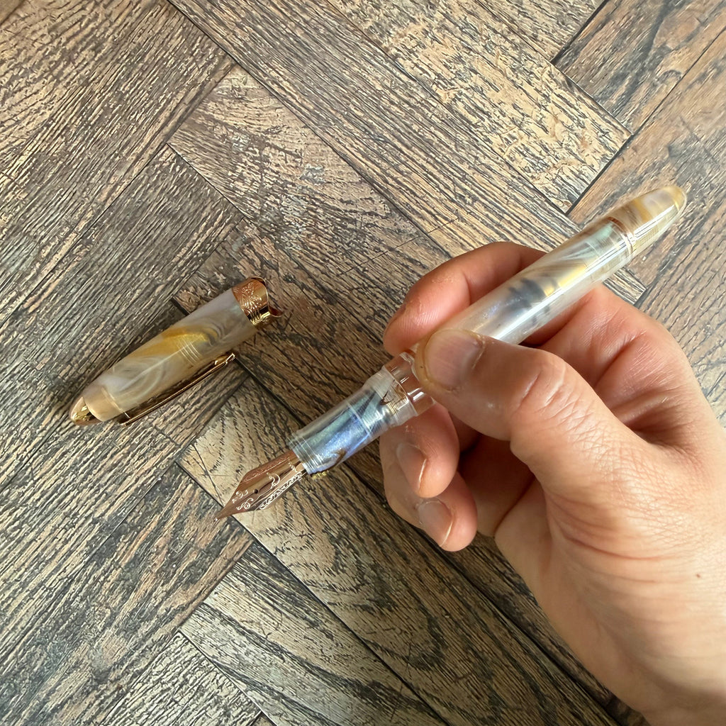 Hand holding the uncapped Nahvalur Horizon Pearl fountain pen, cap resting beside it