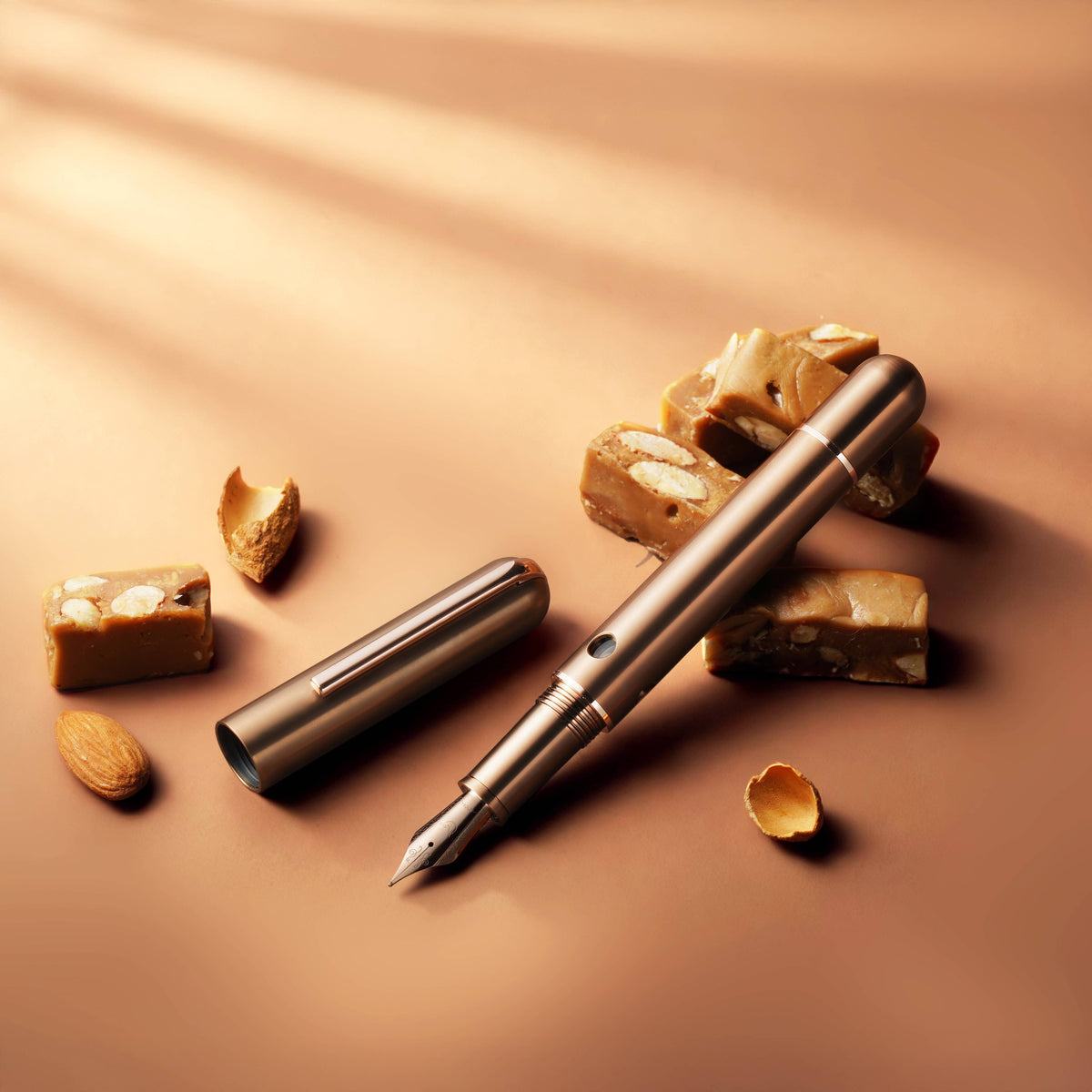 Nahvalur Nautilus Ti Toffee fountain pen and cap lying on a warm tan surface with toffee and almonds