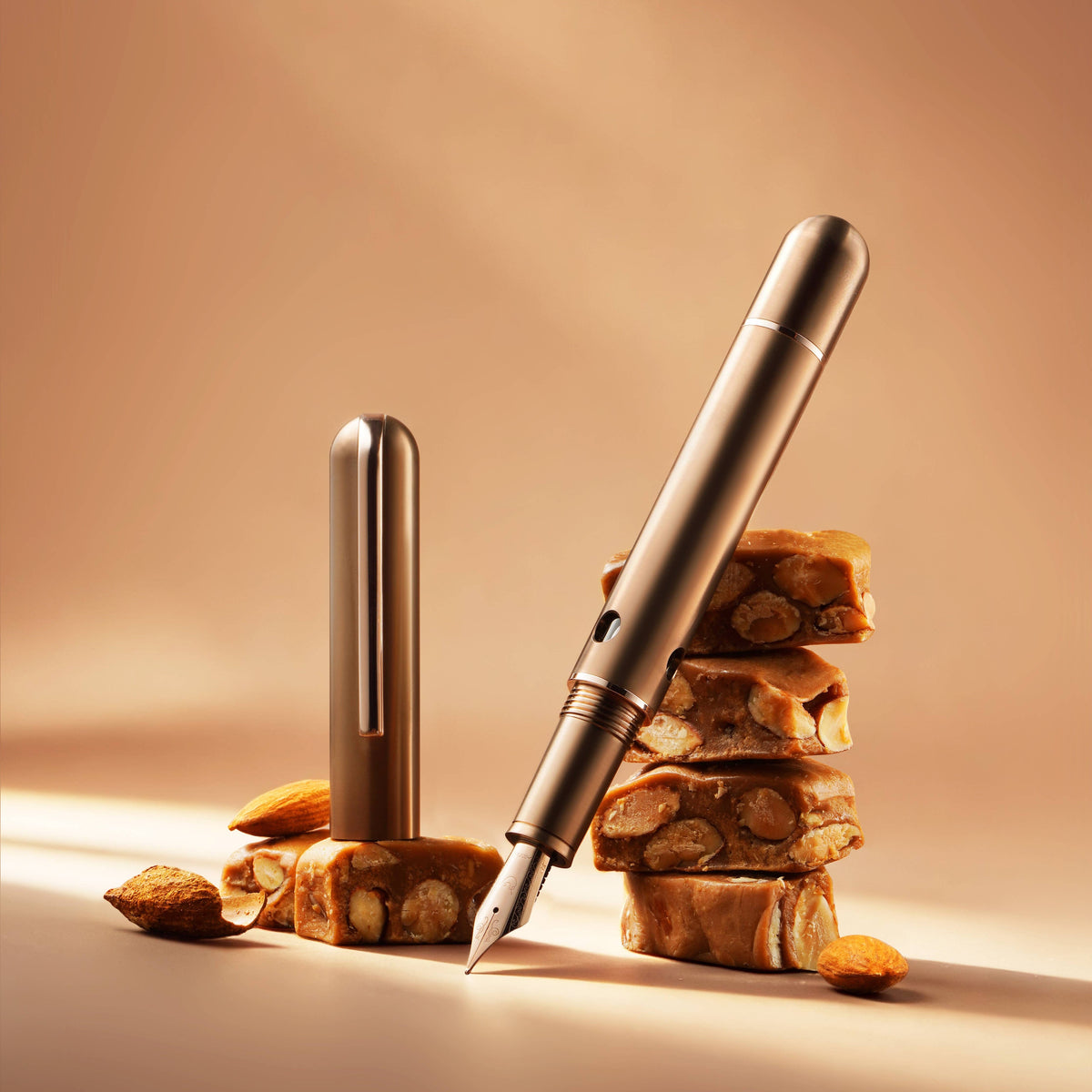 Nahvalur Nautilus Ti Toffee titanium fountain pen leaning on stacked toffee, with its cap beside it