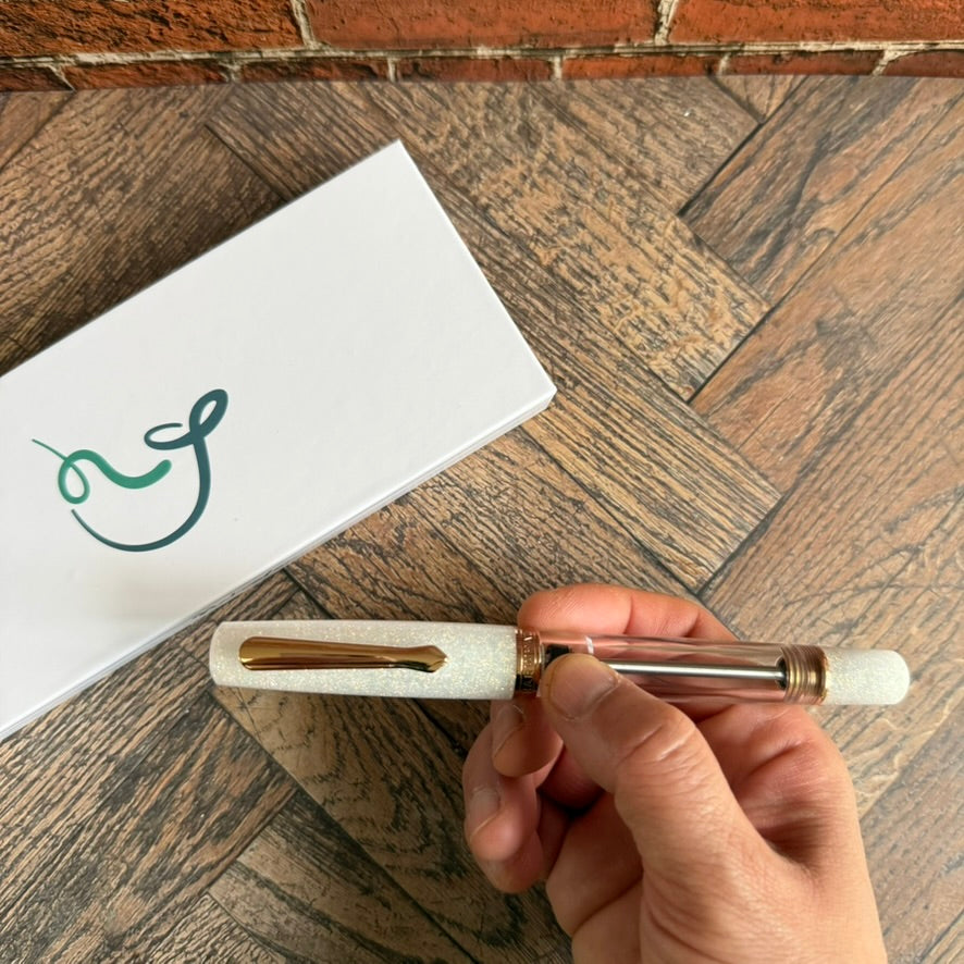 Hand holding the capped Nahvalur Original Plus Matira Quartz fountain pen beside its white Nahvalur gift box