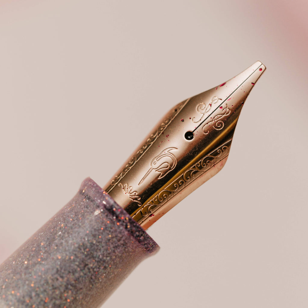 Rose gold Nahvalur nib with scrollwork engraving, shown against a soft pink background