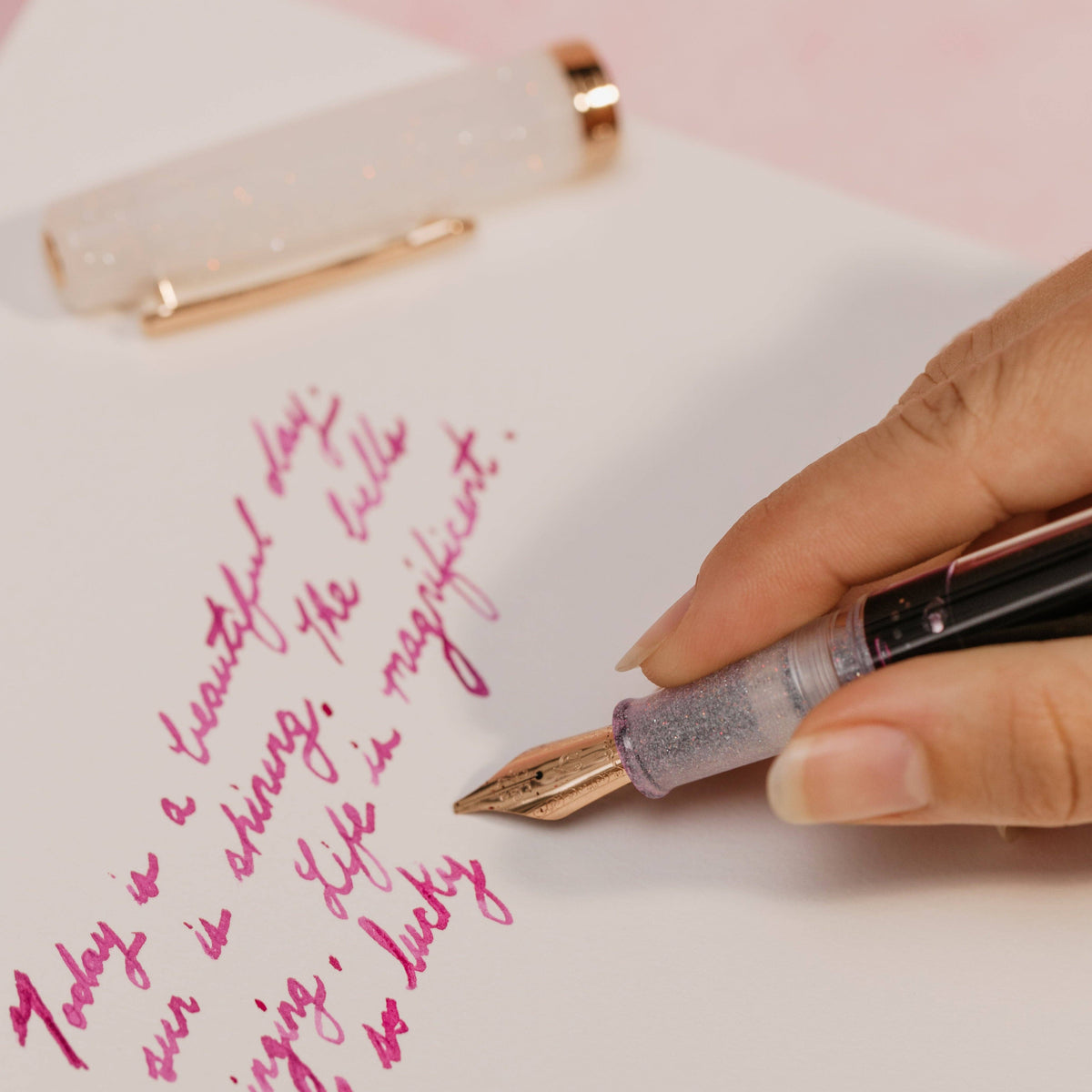 Writing in pink ink with the Nahvalur Original Plus Matira Quartz fountain pen, cap resting on the page