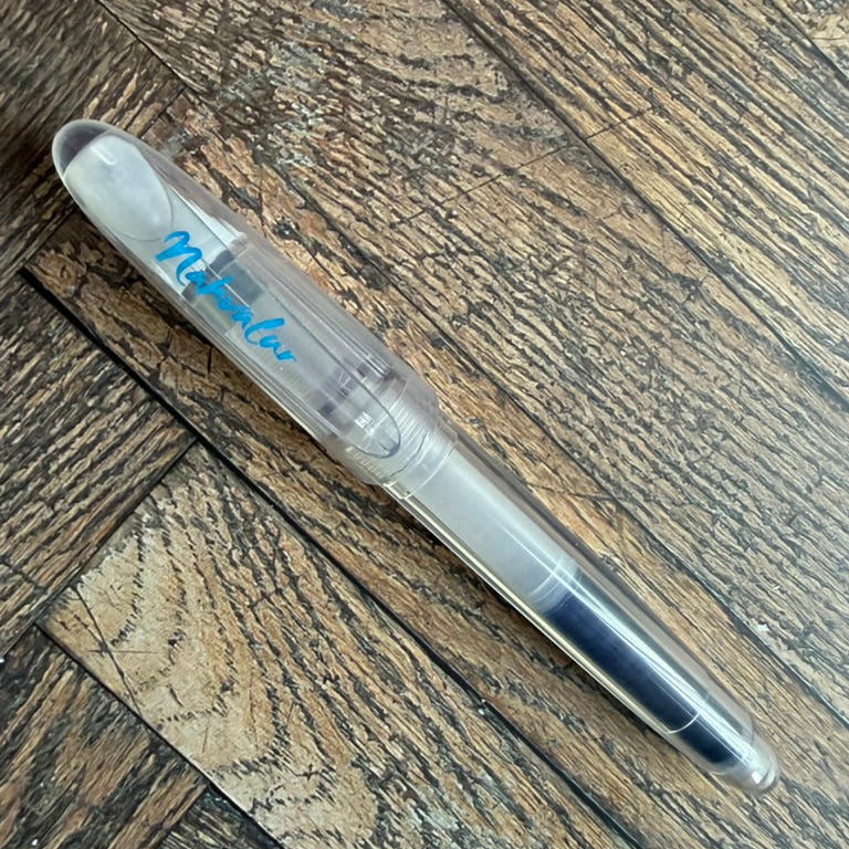 Nahvalur Triad clear demonstrator fountain pen, capped, with blue Nahvalur script on the cap