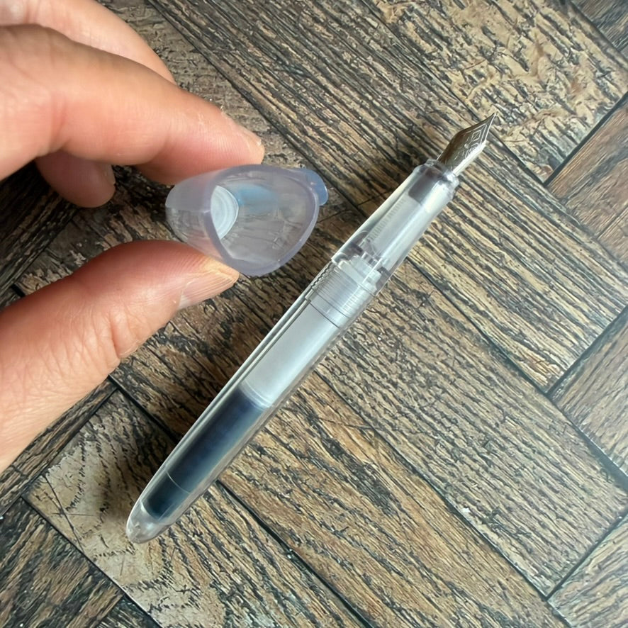 Hand holding the snap cap above the uncapped Nahvalur Triad clear fountain pen