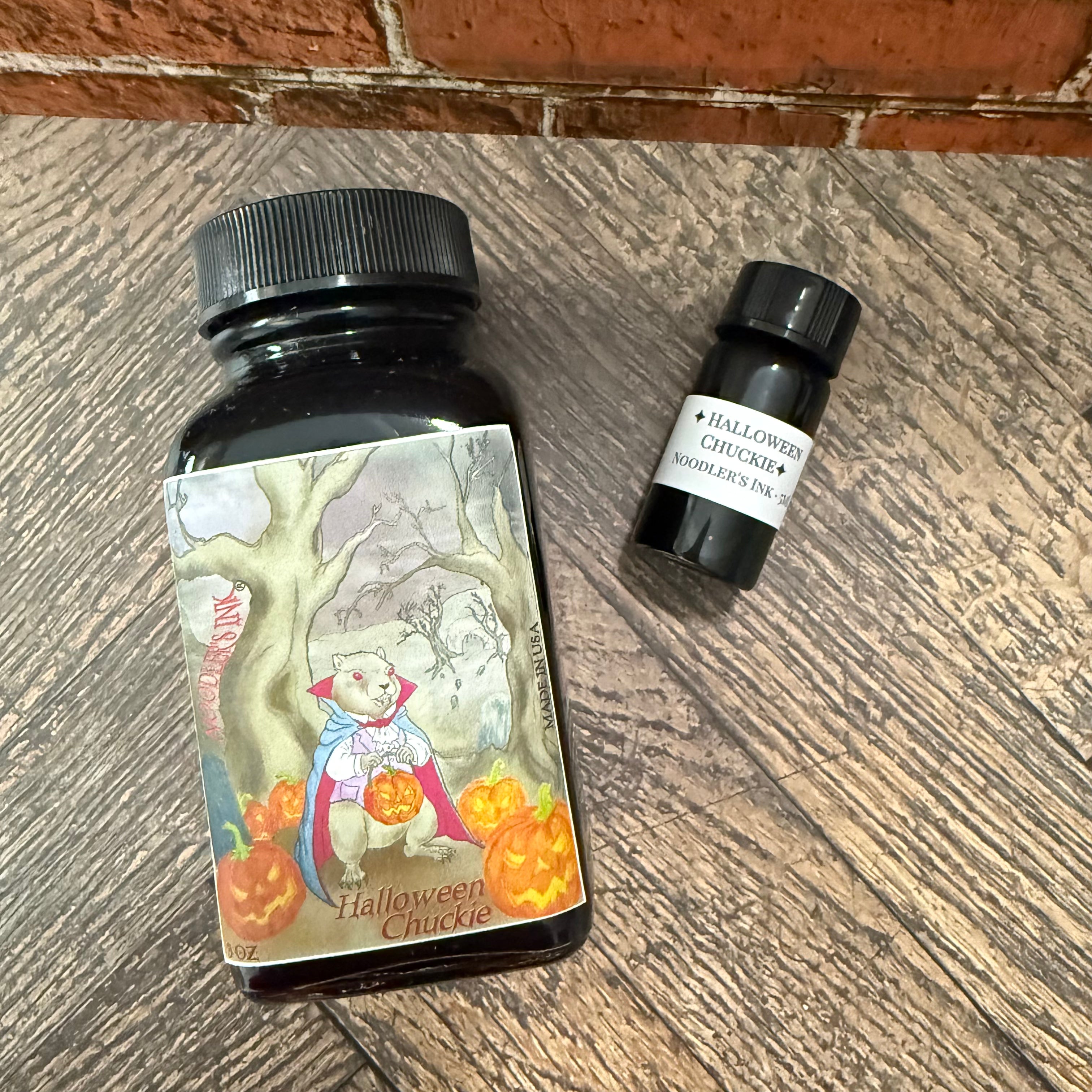 Noodler's Halloween Chuckie full bottle and labeled 5 mL sample vial on a wooden floor