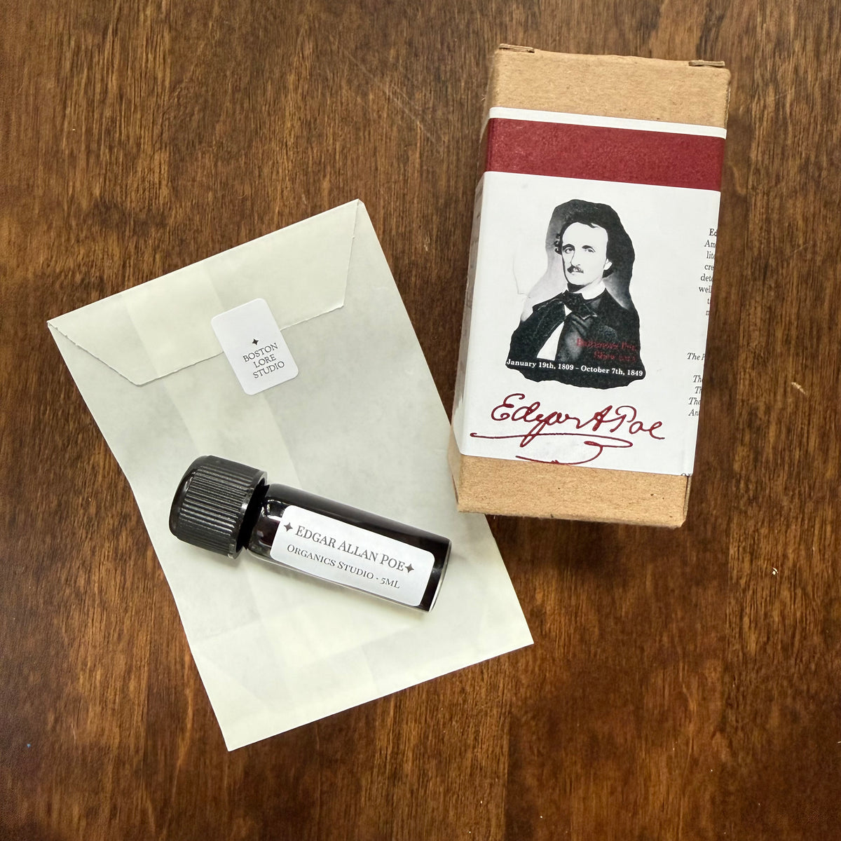 Organics Studio Edgar Allan Poe 5 mL Archive Bottle displayed with a glassine envelope and Poe portrait packaging on a wooden surface